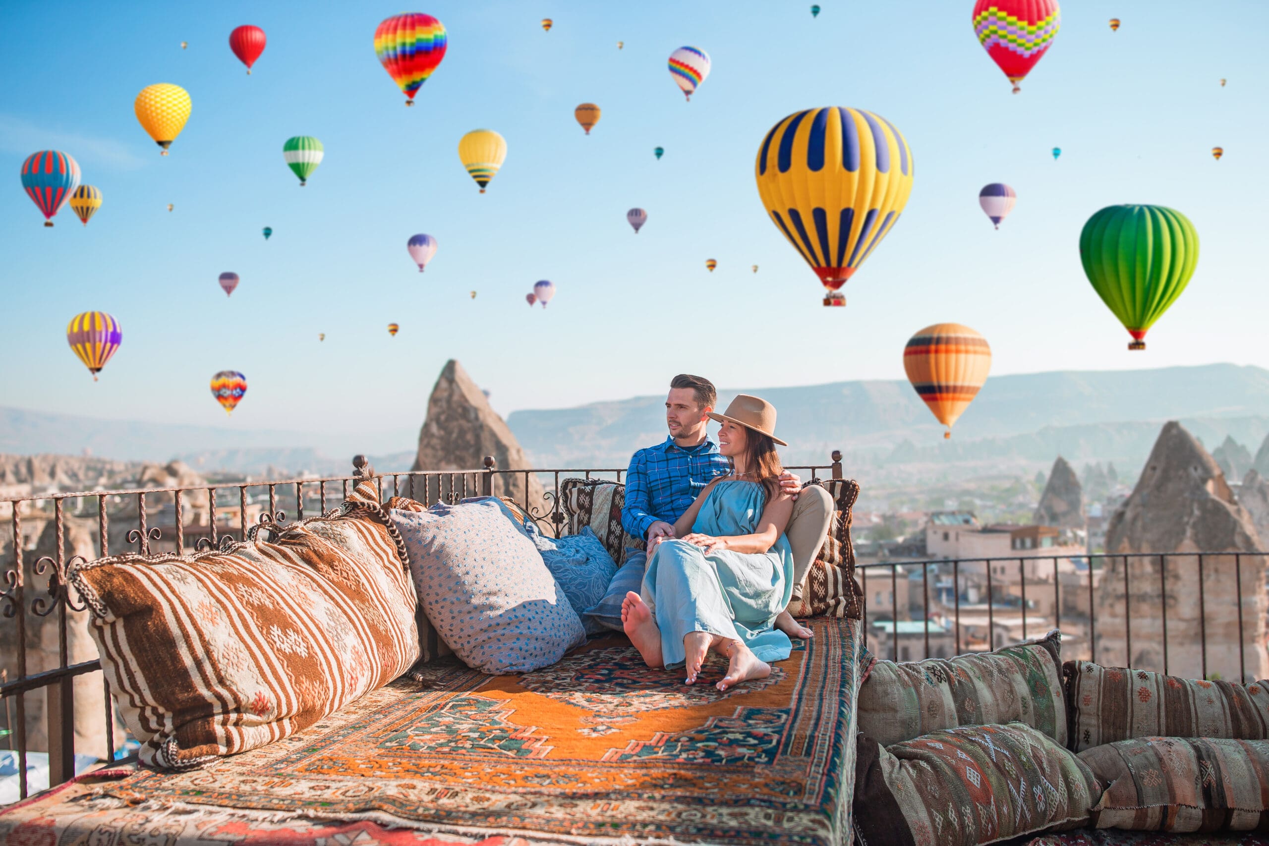 Young couple at sunrise on a rooftop in Cappadocia with hot air balloons in the background. Couple travels the world. Hot air balloon flights.