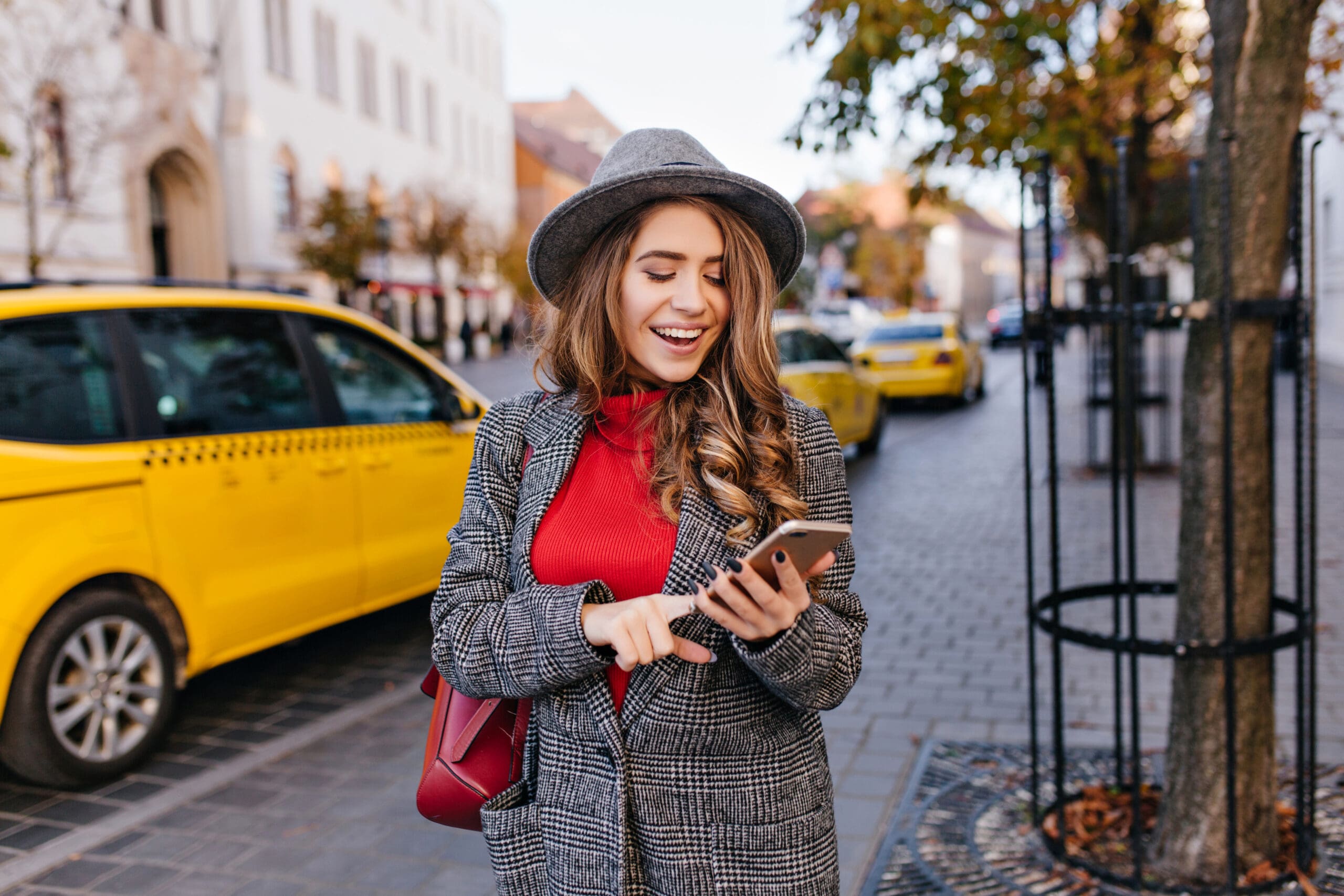 woman texting message while walking on the street. Lady in coat looking at phone screen, standing on avenue with taxi on background.