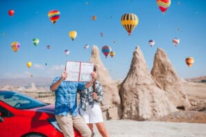 Happy couple on vacation by car in Cappadocia with hot air balloons in the background. Cave formations. Hot air balloon flights.