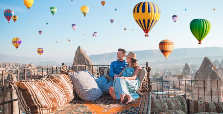 Young couple at sunrise on a rooftop in Cappadocia with hot air balloons in the background. Couple travels the world. Hot air balloon flights.