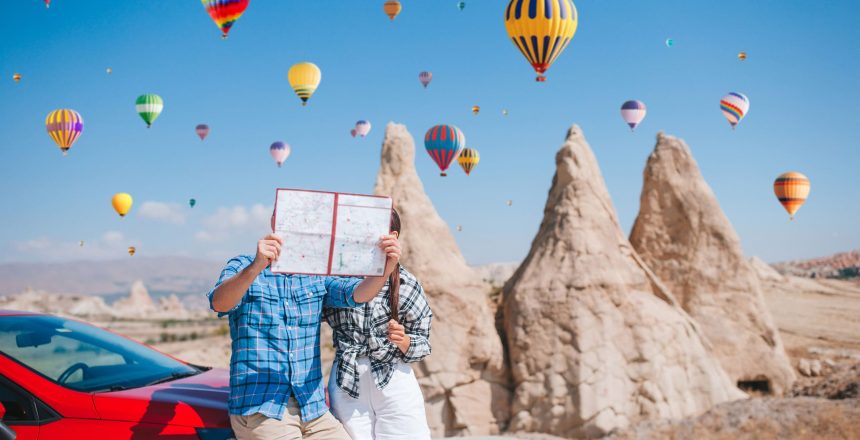 Happy couple on vacation by car in Cappadocia with hot air balloons in the background. Cave formations. Hot air balloon flights.